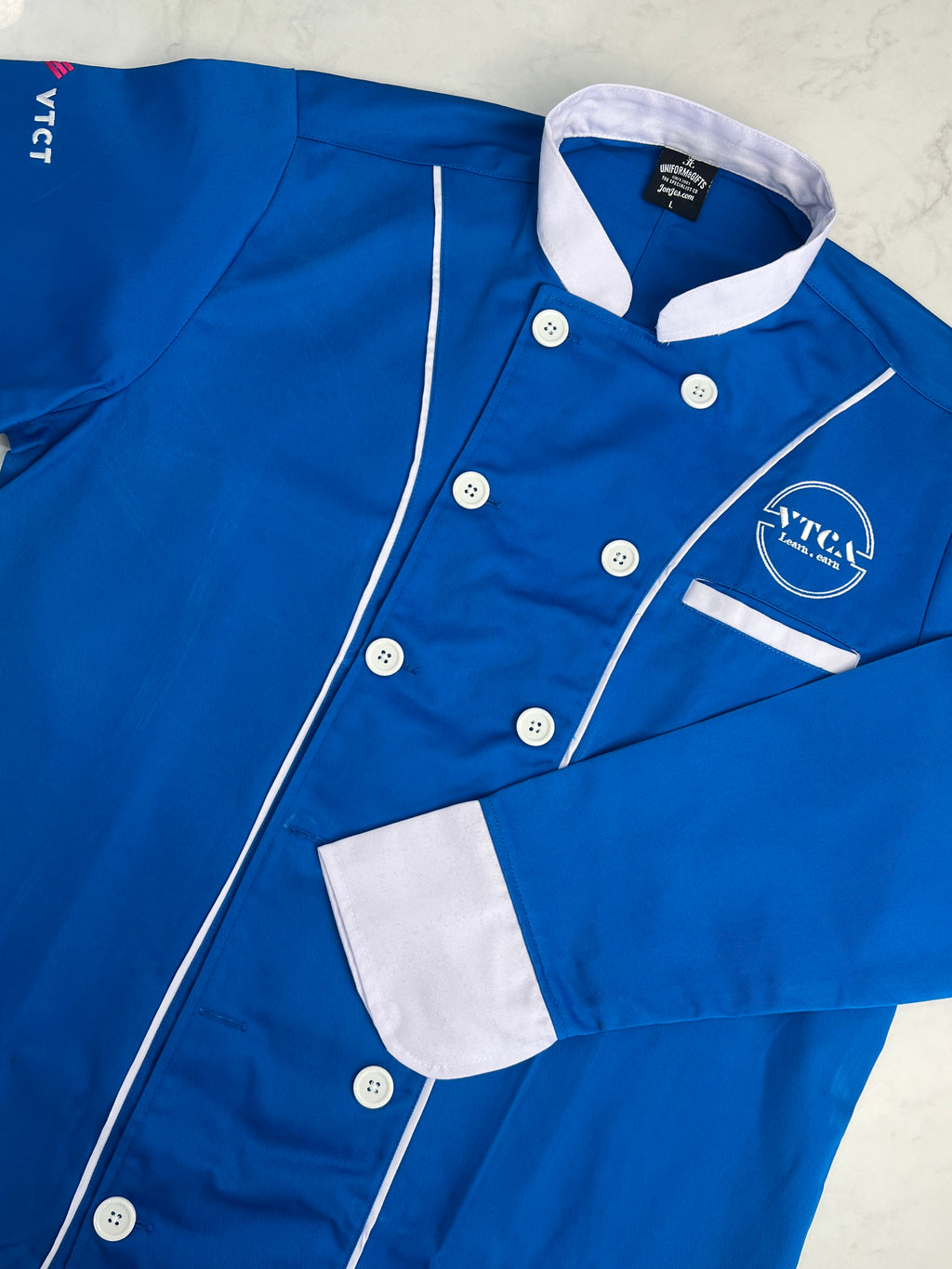 Blue chef's coat with white buttons and trim on a light gray background