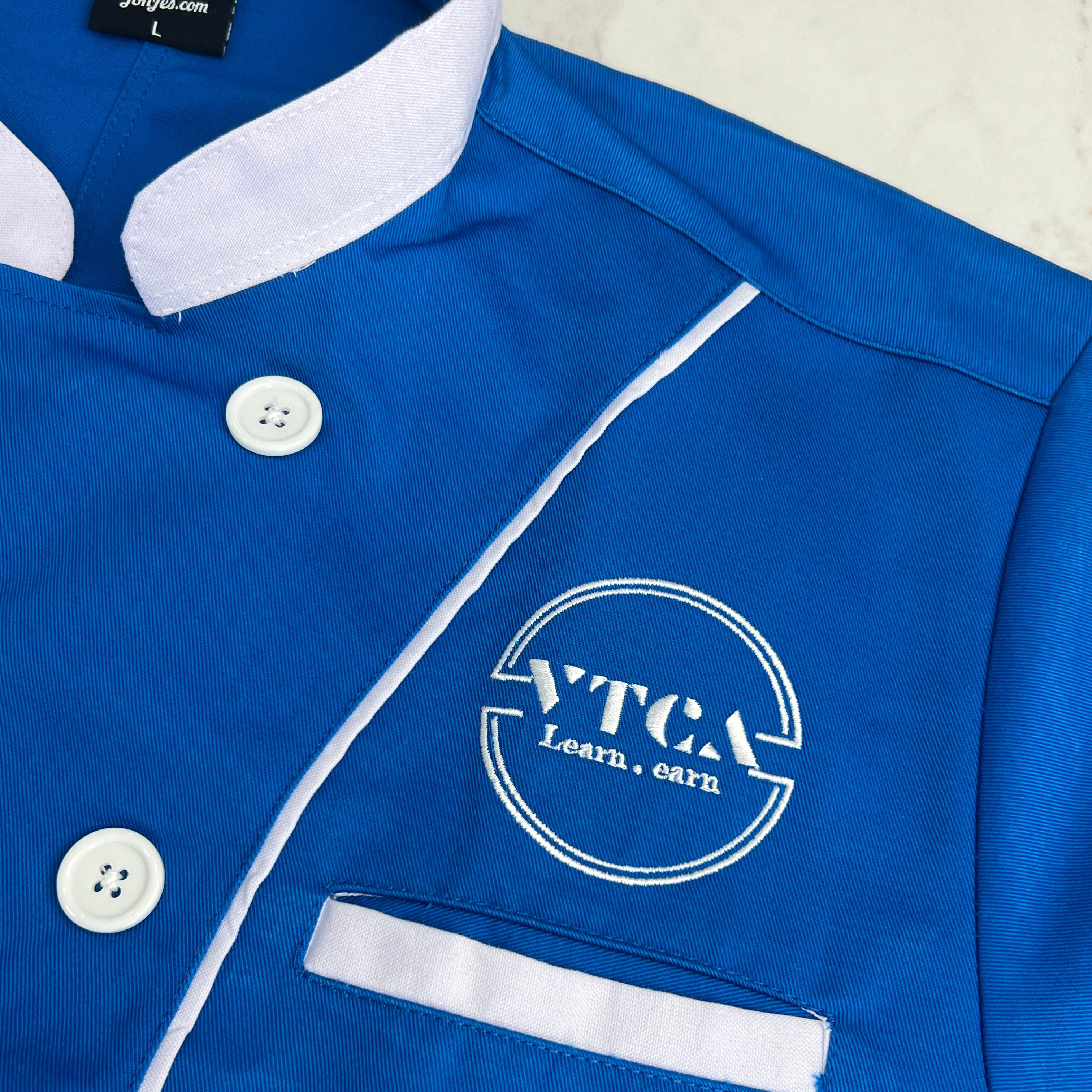Blue jacket with white buttons and VTCA logo on a light background